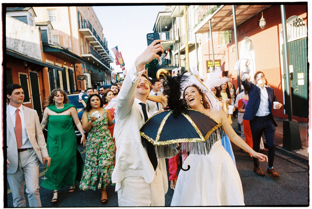 Bride and groom dancing at their new orleans destination wedding and taking a selfie with guests behind them at their second line